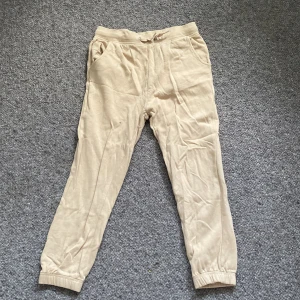 Beige mjukisbyxor - Säljer ett par bekväma beige mjukisbyxor i storlek 157/160. Byxorna har en elastisk midja med snörning och muddar vid bensluten. Perfekta för en avslappnad dag hemma eller för att chilla med kompisar. De är i bra skick och redo för en ny ägare! Köparen betalar för frakt!