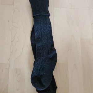 Svarta knä strumpor - Säljer ett par svarta strumpor i nyskick. De är långa och ser ut att vara bekväma med en ribbstickad mudd vid toppen. Perfekta för vardagsbruk eller när du vill hålla fötterna varma. gjorda i 100% bomull
