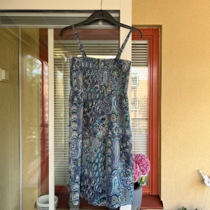 Sommarklänning från Esprit Collection - Säljer en söt klänning från Esprit. Möstret är i olika blå nyanser. Endast använd handfull ggr. Avtagbara axelband. Fodrad med blått tyg. Bred resår över byst. Omkrets ca 68 cm (ostretchad). Längd ca 72 cm. Medföljer band att sätta i midjan. 
