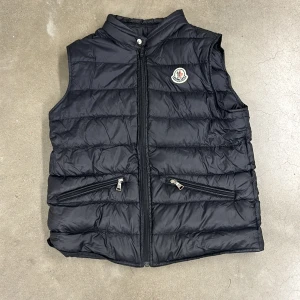 Moncler väst - Säljer min Moncler väst för att den är för liten för mig, det är i väldigt bra skick förutom att kedjan är utbytt men man ser bara det från kort hål, skriv om ni har några funderingar!