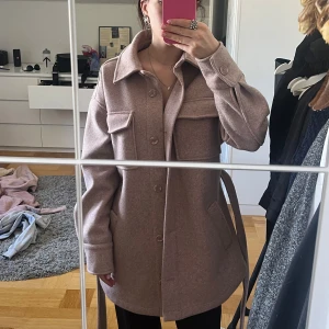 Rosa kappa med bälte från Bik Bok - Säljer en smuts rosa kappa från BikBok i storlek XS. Pågurnd av ett den inte kommit till användning. Kappan är i en ullblanding, därför perfekt till höst eller vinter.