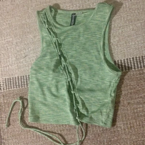 Grön ribbad linnetopp från Cubus - Säljer en snygg grön ribbad linnetopp från Cubus. Toppen är ärmlös och har en cool snörningsdetalj på framsidan som ger den en unik look. Perfekt för sommaren eller en festkväll! 💚