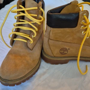 Bruna kängor från Timberland - Säljer ett par bruna kängor från Timberland i storlek herr 42. De är gjorda av skinn och har en robust sula som ger bra grepp. Skorna har gula snören och en vadderad svart krage för extra komfort. Perfekta för höst och vinter!