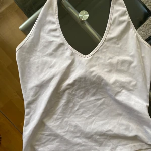 Vit ärmlös linnetopp - Säljer en vit ärmlös linnetopp. Toppen har en djup v-ringning och är tillverkad i ett mjukt och bekvämt Silk material. Perfekt för sommaren eller som ett basplagg i garderoben. Toppen är i finskick och har en tight passform.