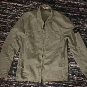 Grön overshirt från Stone Island - Säljer en snygg grön overshirt från Stone Island. Den har en dragkedja framtill och patch på ärmen. Perfekt för vår och höst. Jackan är i bra skick🔥