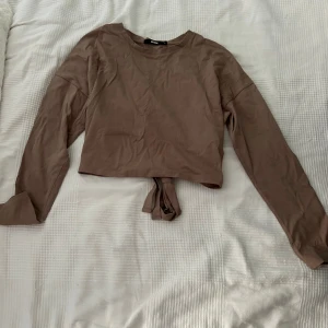Brun croppad topp från BikBok - Säljer en snygg brun croppad topp från BikBok. Den har långa ärmar och en knytning på baksidan.