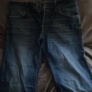 Blå jeans från Jack & Jones - Säljer ett par snygga blå jeans från Jack & Jones. De har en klassisk femficksdesign och knappar i gylfen. Perfekta för en avslappnad stil och passar till det mesta. Jeansen är i bra skick och redo för en ny ägare!