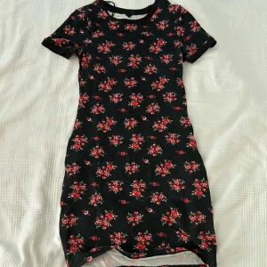 Svart blommig klänning från H&M Divided - Säljer en superfin svart klänning från H&M Divided med ett gulligt blommönster i rött. 