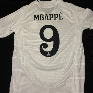 Mbappe Real Madrid tröja - En mycket fin Mbappe Real Madrid hemma tröja 2024/25! Helt ny och oanvänd! Tröjan har UCL patch på ärmen och är Player Version! Hör av dig vid frågor :)