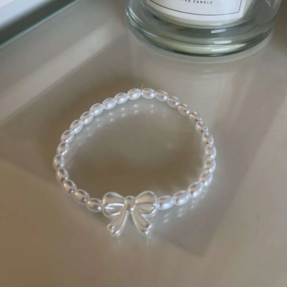 Säljer ett superfint armband med vita pärlor och en söt rosett. Perfekt för att ge en elegant touch till vilken outfit som helst. Passar både till vardags och festliga tillfällen!. Accessoarer.