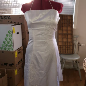 Vit klänning men blommor - Bra skick. Använd som bröllopsklänning. Blommönster på framsidan. Dragkedjan på sidan funkar fint, fick inte upp den när den satt på dockan dock. 