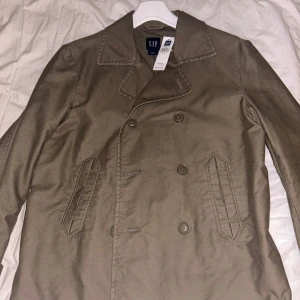 Kort trenchcoat i stl L - Ny trenchoat i tjockare material i stl L. Aldrig använd med prislapp kvar. Köptes för ca 1000kr. 