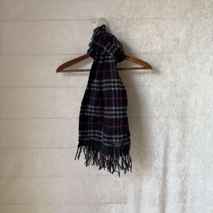 burberry halsduk - Säljer en halsduk från Burberry. Den är i en stilren kombination av blått, grått och rött.  Perfekt för att hålla sig varm under höst och vinter. Gjord i mjukt lammull material som känns lyxigt mot huden. Passar både till vardags och festliga tillfällen! Passar nu under vintern och hösten. Skicket är 9/10 utan defekter och såklart äkta👍 hör av er vid funderingar👍