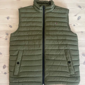 Tommy Hilfiger Väst - Kondition 10/10, den sitter riktigt bra! använd en gång- kom som present men behöver inte den. Kommer med en liten väska ifall den tar upp för mycket plats. Tunn men varm och vattentät. Snygg färg också. Fråga om det är något!