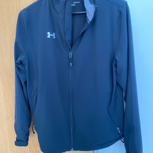 Golf-vindjacka, svart Under Armour, stl YLG - Jättefin, knappt använd, svart Golf-vindjacka med helt blixtlås fram,från Under Armour, i stl YLG (passar 10-13 år), nypris ca 850kr, nu endast 500kr! 