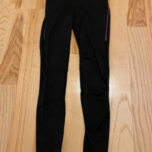Svarta träningsleggings med dragkedja - Säljer ett par svarta träningsleggings. De har en tight passform och är perfekta för träning/löpning. Byxorna har praktiska dragkedjor vid bensluten baktill med reflexer, så du syns i mörkret, och en liten ficka med dragkedja. 