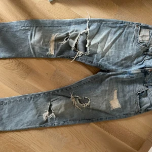 Blå slitna jeans från Zara Boyfriend  - Säljer ett par blå jeans från Zara i storlek 34. De har en cool, sliten look med flera revor och slitningar på benen. Perfekta för en avslappnad och trendig stil. Passar bra till både vardag och fest! Passar s-m 