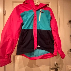 Färgglad vindjacka från McKinley - Säljer en supercool vindjacka från McKinley i storlek 160. Den har en härlig mix av färger med rosa, turkos och mörkblå. Jackan har en dragkedja framtill och en praktisk huva. Perfekt för vår och höst när vädret är lite ostadigt. Passar både för skolan och fritidsaktiviteter!