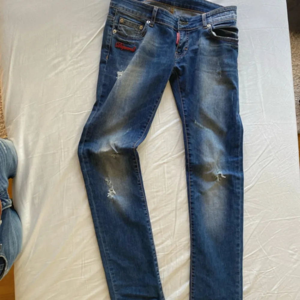 Säljer ett par snygga blå jeans från Dsquared2. De har en fet slitning och broderad logga på framsidan. Jeansen är tillverkade i Italien och har en klassisk femficksdesign. Perfekta för en avslappnad men stilren look! Nyskick! Storlek w28 l32.. Jeans & Byxor.