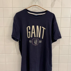 T-shirt GANT - Storlek M - Säljer en blå T-shirt med tryck från GANT i storlek M. T-shirten är i bra, använt skick och perfekt för en avslappnad och stilren look.