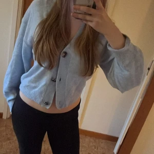 Ljusblå kofta med knappar - Säljer en superfin ljusblå kofta som är perfekt för både vår och höst. Den är croppad och har stora, snygga knappar framtill. Materialet känns mjukt och skönt, perfekt för att hålla sig varm men ändå se stilren ut. Passar perfekt till ett par jeans eller leggings!