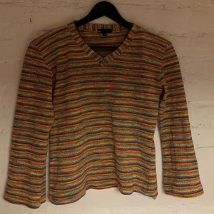 Flerfärgad randig tröja från att. - Säljer en färgglad randig tröja från att. Tröjan har en v-ringad hals och långa rätt vida ärmar. Perfekt för att liva upp garderoben med sina glada färger till våååren