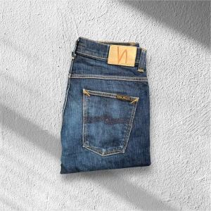 Mörkblå Nudie Jeans Grim Tim – W33 L32 - Säljer ett par mörkblå Nudie Jeans i modellen Grim Tim, storlek W33 L32. Jeansen är i mycket fint skick med minimal användning. En stilren och bekväm slim-fit modell i hög kvalitet som funkar perfekt både till vardag och mer uppklädda tillfällen!