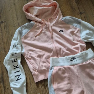 Rosa vit hoodie tracksuit Nike Air - Säljer en snygg rosa och vit tracksuit från Nike Air. Ärmarna är långärmade med ett tryck av 'NIKE AIR' på ena ärmen. Perfekt för en sportig look! Märkt xs, passar perfekt på S