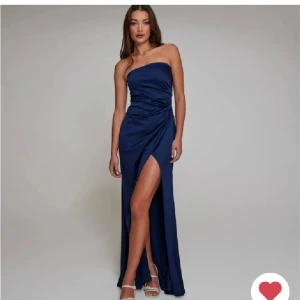 Marinblå axelbandslös långklänning - Elegant marinblå långklänning med en axelbandslös design och en smickrande slits framtill. Klänningen har en draperad detalj vid midjan som ger en fin silhuett. Perfekt för en festlig kväll. Använd endast en kväll. Lite sliten i släpet