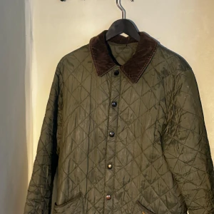 Olivgrön quiltad lång jacka från Barbour - Brun manchestertyg på kragen. Lite längre design, går ungefär till toppen av låren Perfekt för höst och vår.
