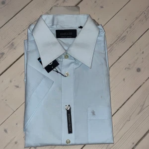 Ljusblå skjorta från Greggio - Snygg ljusblå skjorta från Greggio med klassisk krage och knappar framtill. Perfekt för en stilren look. Skjortan är tillverkad i ett mjukt material som ger en bekväm passform.