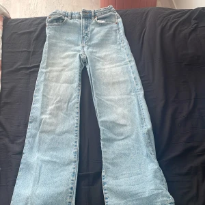 Ljusblå jeansbyxor - Säljer ett par ljusblå jeansbyxor med klassisk femficksdesign och knappgylf. Byxorna har en rak passform och är perfekta för en avslappnad stil. De är tillverkade i ett slitstarkt denimtyg.