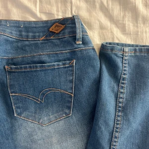 Blå jeans från Lee Cooper - Snygga blå jeans från Lee Cooper med klassisk femficksdesign och knappgylf. De har en straight passform och är lågmidjade! Jeansens blå färg och slitna detaljer ger dem en cool look. Storlek: W28/L32