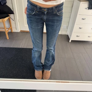 Blå bootcutjeans från Lee - Snygga blå lågmidjade jeans från Lee med klassisk femficksdesign och knappgylf. De har en bekväm passform och är tillverkade i en bomullsblandning med lite stretch för extra komfort. Hör av er om ni har några frågor!💖