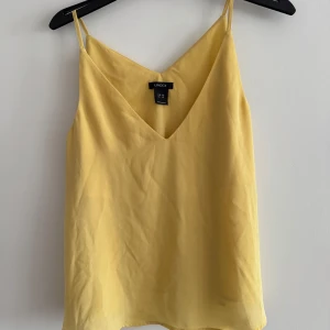 Gul linnetopp från Lindex - Säljer en solgul linnetopp från Lindex med smala axelband och v-ringning. Perfekt för varma sommardagar. Toppen har en lös passform som ger en luftig känsla.