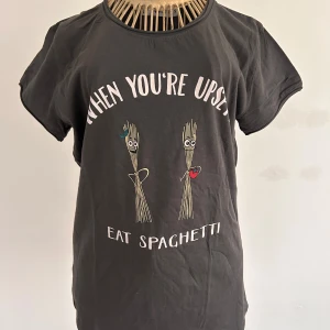 Grå t-shirt med tryck Stl S NY - Säljer en grå t-shirt från FB Sister med ett roligt tryck som säger 'When you're upsetti, eat spaghetti'. T-shirten har korta ärmar och en rund halsringning. Perfekt för en avslappnad stil med en humoristisk touch. Aldrig använd!