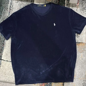 Mörkblå t-shirt från Ralph Lauren - Säljer en stilren mörkblå t-shirt från Ralph Lauren med det klassiska broderade logotypen på bröstet. T-shirten har en normal passform och är tillverkad i ett mjukt material som ger en lyxig känsla. Perfekt för en avslappnad men ändå elegant look. Det går att diskutera om priset!🙃