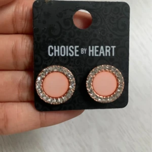 Runda örhängen från Choise by Heart - Snygga runda örhängen från Choise by Heart med en ljusrosa mitt och en glittrig kant i silver. Perfekta för att ge en touch av elegans till din outfit. 💖