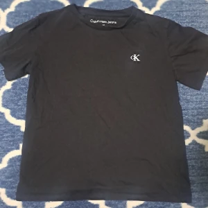 Svart t-shirt från Calvin Klein Jeans - Snygg svart t-shirt från Calvin Klein med liten CK-logga på bröstet. Den har en klassisk design med korta ärmar och rund hals. Perfekt för en stilren look.