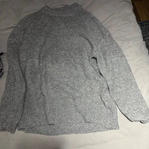 Grå stickad tröja - Säljer en mysig grå stickad tröja med långärmad design. Perfekt för kyligare dagar och ger en avslappnad look. Tröjan har en enkel och stilren design som passar till det mesta. Perfekt för höst och vinter!