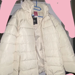 Vit pufferjacka med dragkedja - Säljer en stilren vit pufferjacka från Beverly Hills Polo Club. Jackan har en praktisk dragkedja framtill och är perfekt för kyligare dagar. Den är vadderad för extra värme och komfort.