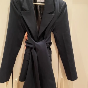 Marinblå kavaj från NA-KD - Jättesnygg marinblå kavaj med knyte från NA-KD i storlek 36. Tyvärr är den för liten för mig. Passar jättebra att ha över en klänning eller topp på våren och sommaren och är inte fodrad!💗