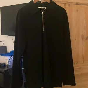 Svart quarter zip från Weekday - Säljer en svart quarter zip från Weekday med dragkedja framtill. Tröjan har långa ärmar och en klassisk krage, perfekt för en minimalistisk look. Passar bra till både jeans och chinos.