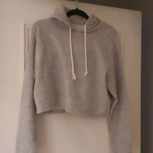 Grå croppad hoodie från H&M Divided - Säljer en grå croppad hoodie från H&M Divided. Den har en justerbar huva med vita snören och långa ärmar. Perfekt för en avslappnad stil. 🩶