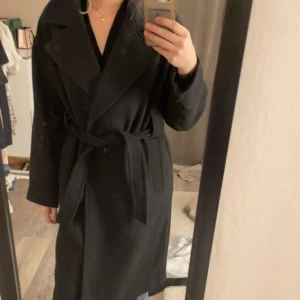 Svart kappa från Vero Moda - Snygg svart kappa med bälte. Perfekt för höst- eller vårsäsongen med sin långa design och klassiska snitt. Köpte för ungefär 600kr för 1/2 år sedan men den har aldrig kommit användning för mig. Hoppas den kommer till användning hos någon annan! 