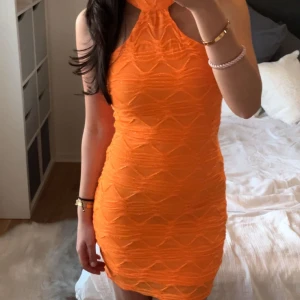 Orange klänning från ginatricot  - Snygg orange klänning med ett unikt mönster och halterneck-design. Perfekt för en somrig look med sin korta längd och figurnära passform.