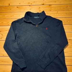 Mörkblå tröja från Ralph Lauren - Säljer en stilren mörkblå tröja från Ralph Lauren med dragkedja vid halsen och det klassiska röda logotypbroderiet på bröstet. Perfekt för en avslappnad och snygg look.