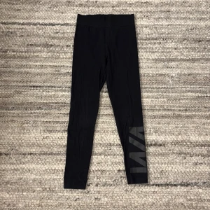 Svarta leggings från Warp - Snygga svarta leggings från Warp med en bred resår i midjan för extra komfort. De har en stilren design med ett diskret tryck på benet. Perfekta för en avslappnad stil.🌺