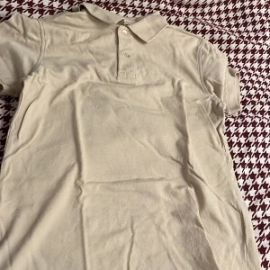Beige pikétröja från Dressmann - Säljer en stilren beige pikétröja från Dressmann i storlek S. Tröjan är tillverkad av 100% bomull och har en klassisk krage med knappar framtill. Perfekt för en avslappnad och snygg look.