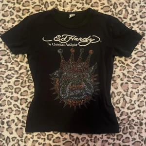 Svart Ed Hardy t-shirt - Snygg svart t-shirt från Ed Hardy med ett stort, glittrigt motiv på framsidan. Texten 'Ed Hardy By Christian Audigier' finns både fram och bak. Sitter som en storlek M. En del rhinestones har ramlat av.